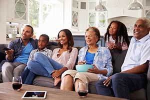 A multi generational family sitting on a sofa while watching TV.